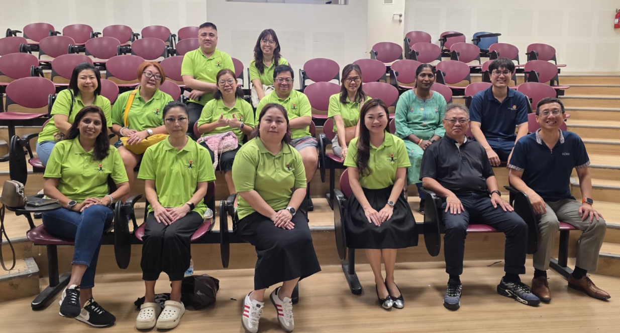 A group of people sitting in an auditorium, most wearing green t-shirt as they are the PSG members